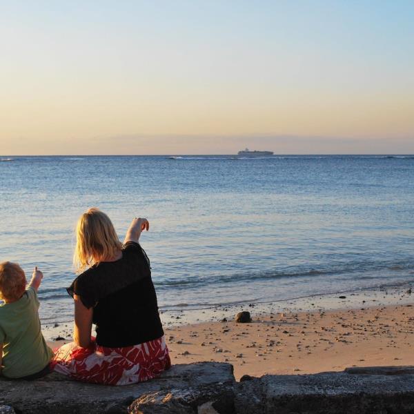 En mor og et barn sitter på stranda og peker utover havet.