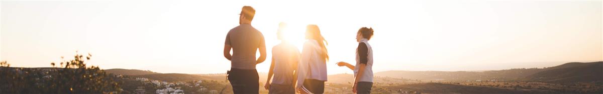 Fire unge voksne med ryggen til kamera ute i naturen. Sola er lavt på himmelen og skinner for hodene deres delvis. - Klikk for stort bilde